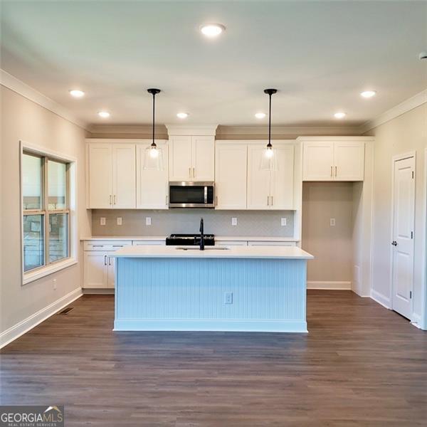 kitchen with a center island with sink, decorative light fixtures, white cabinets, and sink