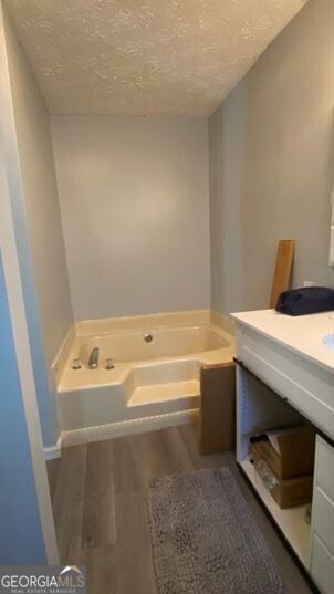 bathroom with a textured ceiling, wood-type flooring, and a bath