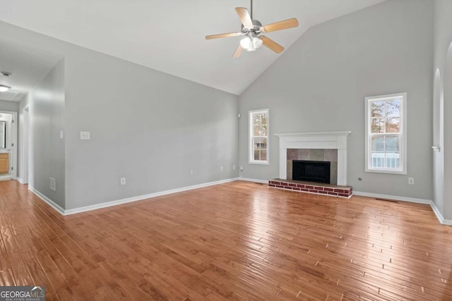 unfurnished living room featuring ceiling fan, wood-type flooring, high vaulted ceiling, and a brick fireplace