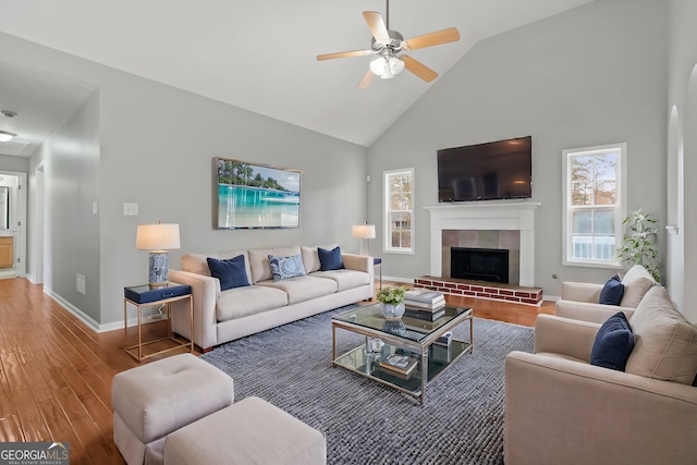 living room with ceiling fan, wood-type flooring, a fireplace, and high vaulted ceiling