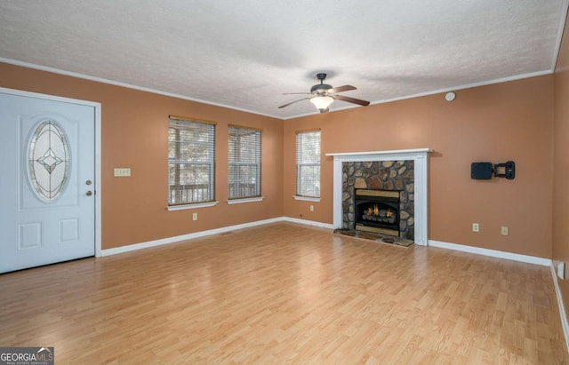 unfurnished living room with a stone fireplace, ceiling fan, ornamental molding, a textured ceiling, and light hardwood / wood-style floors