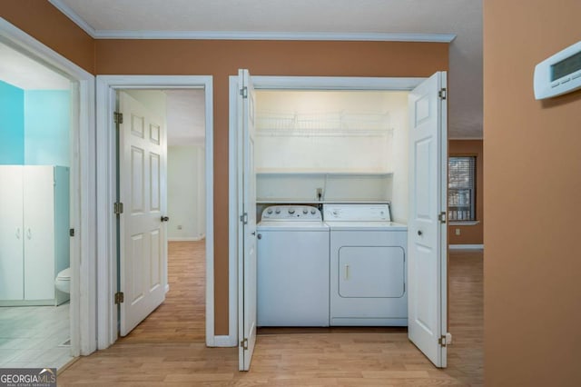 washroom featuring light wood-type flooring, washing machine and dryer, and ornamental molding