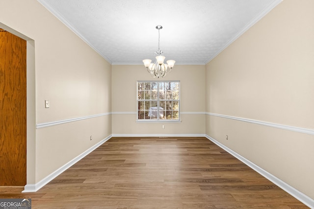 unfurnished dining area featuring wood-type flooring, a textured ceiling, crown molding, and an inviting chandelier