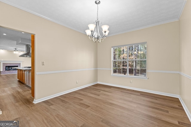 empty room with light hardwood / wood-style floors, crown molding, a notable chandelier, and a fireplace