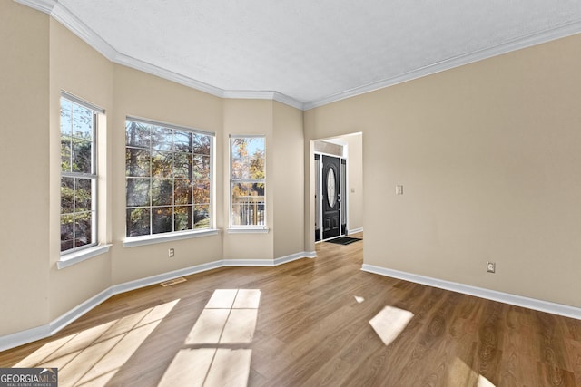 spare room with light wood-type flooring, crown molding, and a textured ceiling