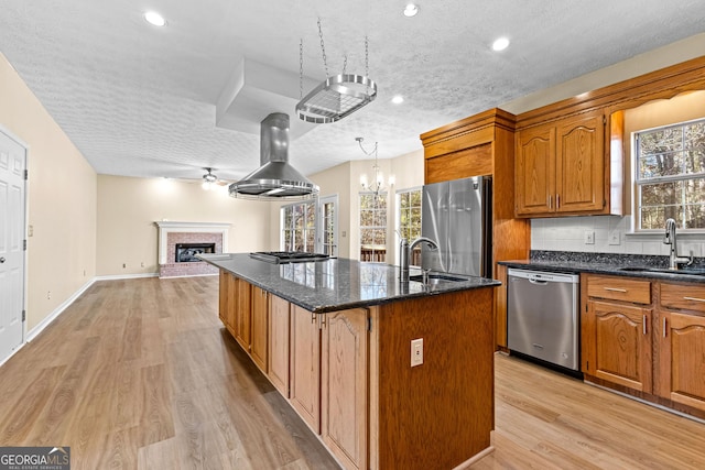 kitchen with light wood-type flooring, a kitchen island with sink, appliances with stainless steel finishes, and a textured ceiling