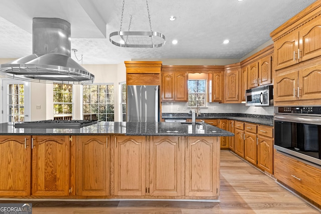 kitchen with a wealth of natural light, island range hood, stainless steel appliances, and an island with sink