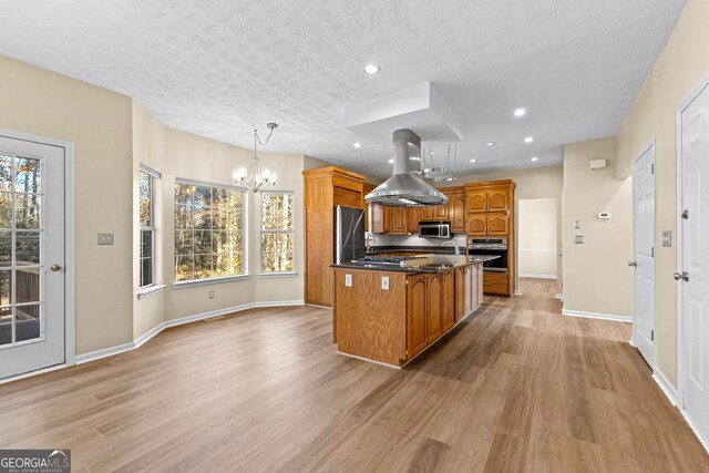 kitchen with a textured ceiling, appliances with stainless steel finishes, a center island, hanging light fixtures, and island range hood