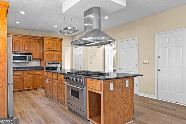 kitchen with light hardwood / wood-style floors, island exhaust hood, stainless steel appliances, decorative backsplash, and a kitchen island with sink