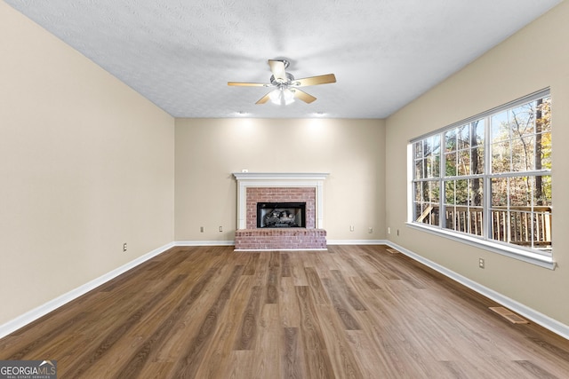 unfurnished living room featuring a brick fireplace, hardwood / wood-style floors, a textured ceiling, and ceiling fan