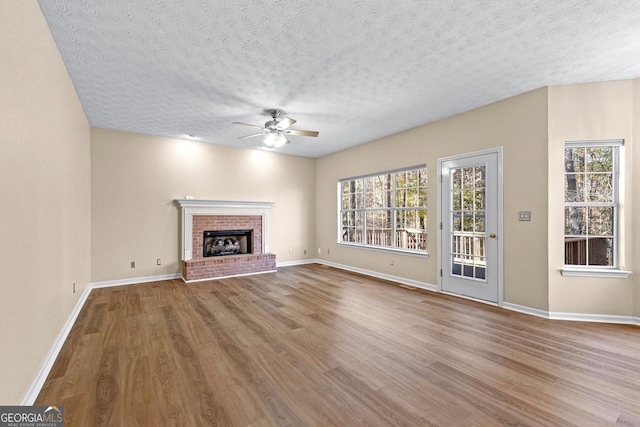 unfurnished living room with ceiling fan, a textured ceiling, light hardwood / wood-style flooring, and a fireplace