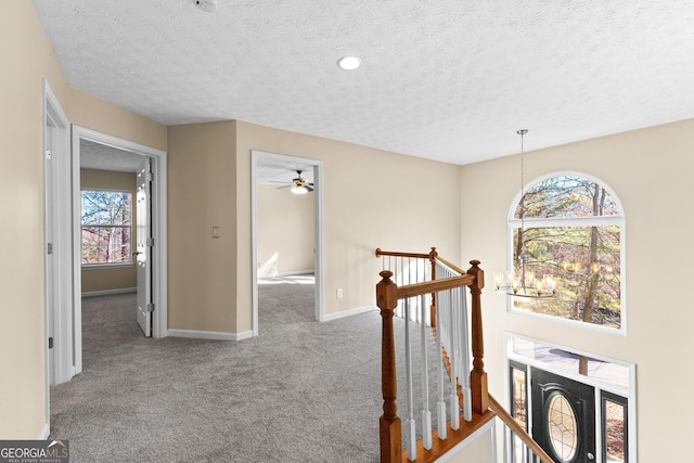 hall with carpet floors, a textured ceiling, and a chandelier