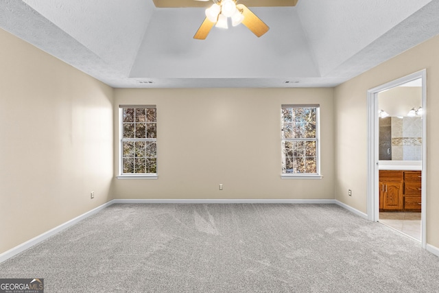 interior space featuring multiple windows, connected bathroom, light carpet, a raised ceiling, and ceiling fan