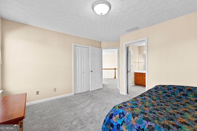 carpeted bedroom with a textured ceiling, ensuite bathroom, and a closet