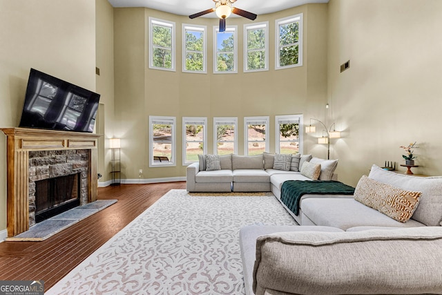 living room with ceiling fan, a fireplace, a towering ceiling, and wood-type flooring