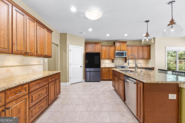 kitchen with backsplash, a kitchen island with sink, hanging light fixtures, sink, and appliances with stainless steel finishes