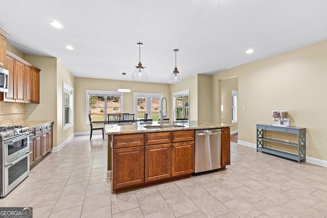 kitchen with a kitchen island with sink, hanging light fixtures, sink, appliances with stainless steel finishes, and light stone counters