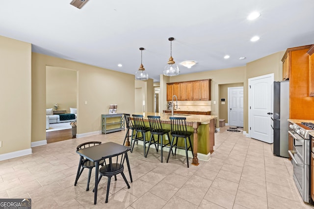 kitchen with a kitchen breakfast bar, stainless steel appliances, a kitchen island with sink, sink, and pendant lighting