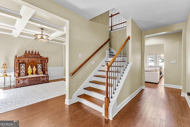 staircase with hardwood / wood-style floors, an inviting chandelier, coffered ceiling, and beam ceiling