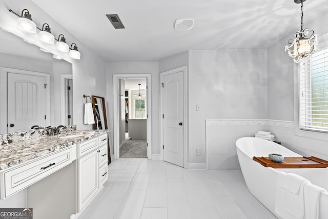 bathroom with tile patterned floors, vanity, tile walls, a notable chandelier, and a tub