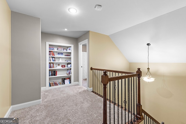 hallway featuring carpet flooring, built in shelves, and lofted ceiling