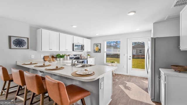 kitchen with stainless steel appliances, a breakfast bar, white cabinets, and kitchen peninsula