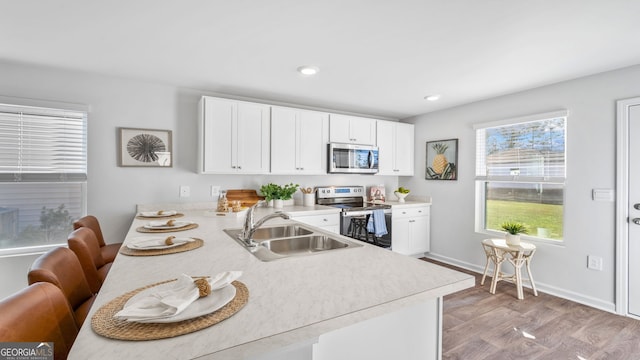 kitchen featuring sink, white cabinetry, light wood-type flooring, appliances with stainless steel finishes, and kitchen peninsula