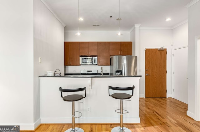 kitchen with a kitchen breakfast bar, stainless steel appliances, decorative light fixtures, and light hardwood / wood-style floors