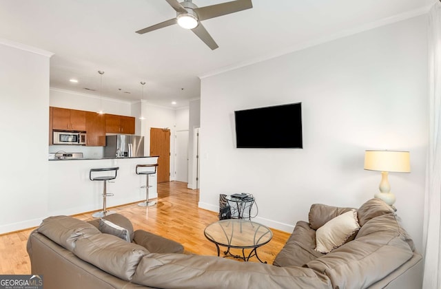 living room with ceiling fan, ornamental molding, and light wood-type flooring