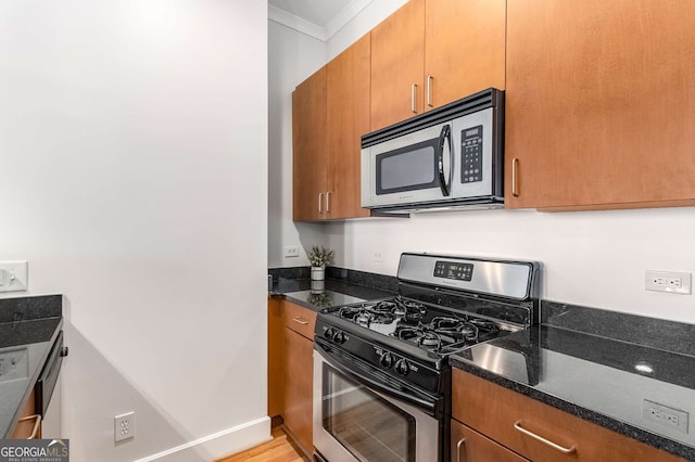 kitchen with ornamental molding, stainless steel appliances, dark stone counters, and light hardwood / wood-style floors