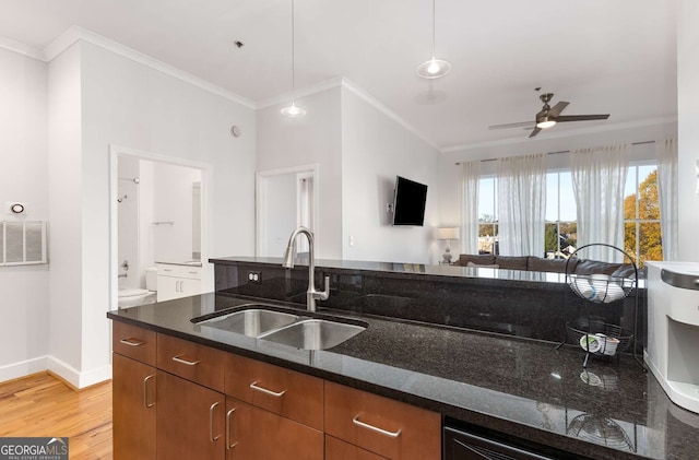 kitchen with ceiling fan, sink, light hardwood / wood-style flooring, dark stone counters, and decorative light fixtures