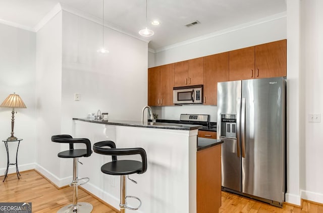 kitchen with kitchen peninsula, stainless steel appliances, hanging light fixtures, and light hardwood / wood-style flooring