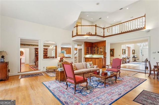 living room with a towering ceiling, light hardwood / wood-style floors, and a notable chandelier