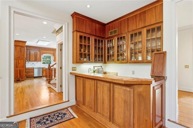 bar with stainless steel dishwasher and light hardwood / wood-style flooring