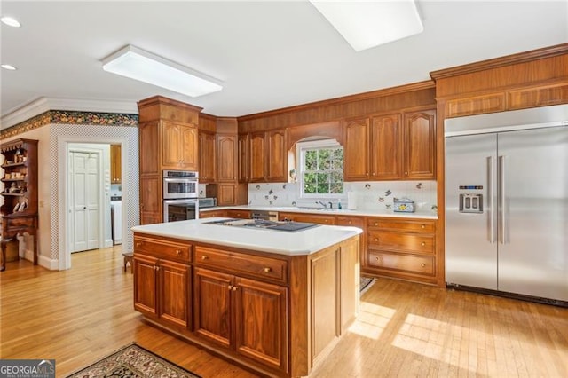 kitchen with sink, appliances with stainless steel finishes, light hardwood / wood-style floors, a kitchen island, and ornamental molding