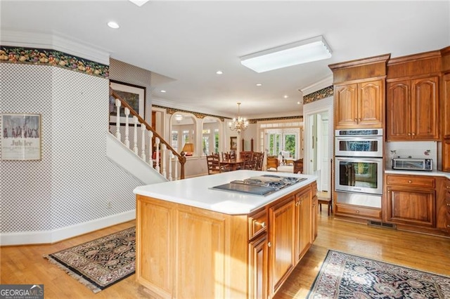 kitchen featuring hanging light fixtures, stainless steel double oven, cooktop, a kitchen island, and light wood-type flooring