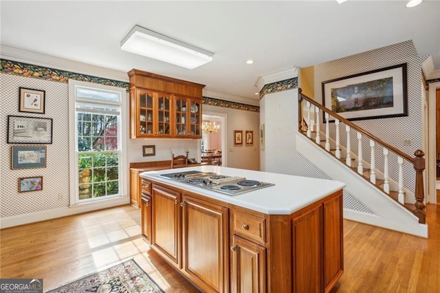 kitchen with light wood-type flooring, a kitchen island, stainless steel gas cooktop, and crown molding