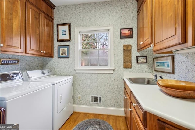 laundry area with washing machine and dryer, cabinets, sink, and light hardwood / wood-style floors