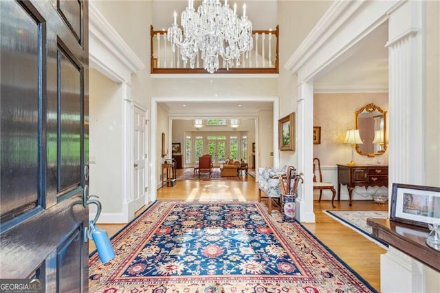 entrance foyer featuring a notable chandelier, light hardwood / wood-style floors, ornamental molding, and a high ceiling