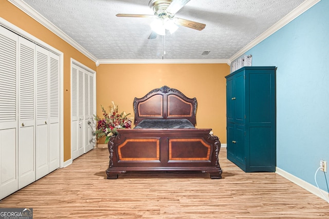 bedroom with two closets, ceiling fan, light wood-type flooring, ornamental molding, and a textured ceiling