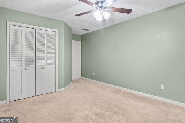 unfurnished bedroom with a textured ceiling, a closet, ceiling fan, and light colored carpet