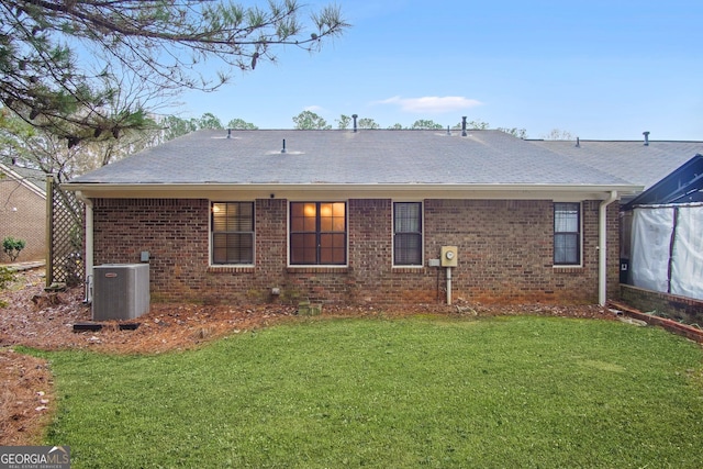 rear view of house with central AC unit and a yard