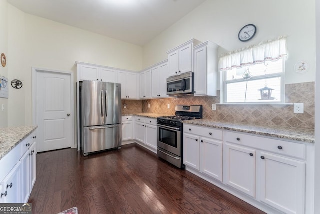 kitchen with backsplash, white cabinets, light stone countertops, appliances with stainless steel finishes, and dark hardwood / wood-style flooring