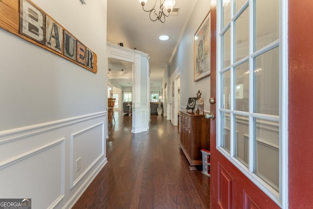 corridor with decorative columns, dark hardwood / wood-style flooring, and an inviting chandelier