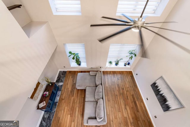 living room featuring a high ceiling, ceiling fan, and wood-type flooring