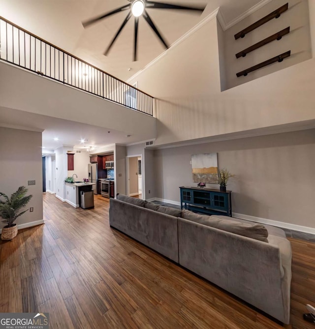 living room featuring sink, ornamental molding, a high ceiling, and hardwood / wood-style flooring