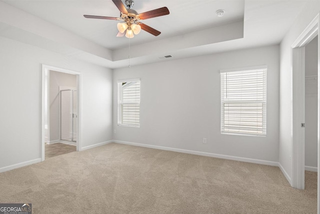 unfurnished bedroom featuring a tray ceiling, ensuite bath, ceiling fan, and light carpet