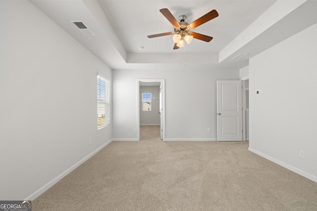 carpeted spare room with a raised ceiling and ceiling fan