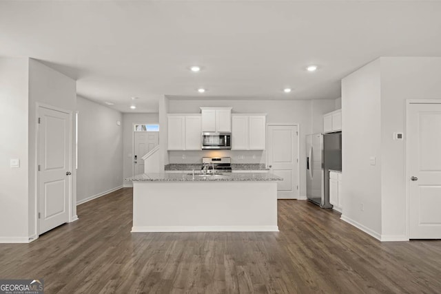 kitchen with white cabinets, appliances with stainless steel finishes, light stone counters, and a kitchen island with sink