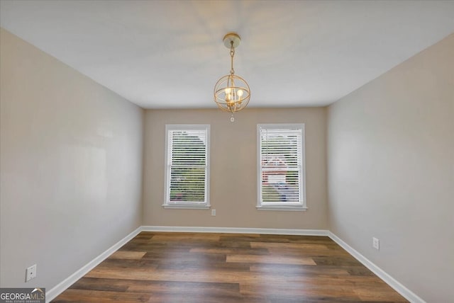 spare room with dark hardwood / wood-style flooring and an inviting chandelier